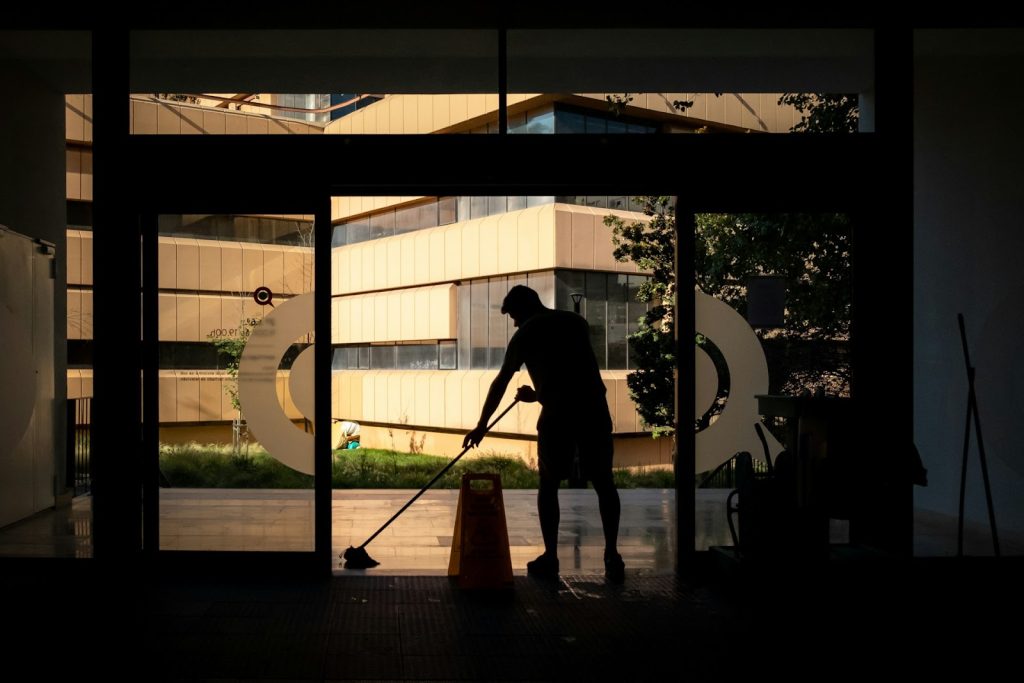 A male cleaner mops a floor by an external door by hand