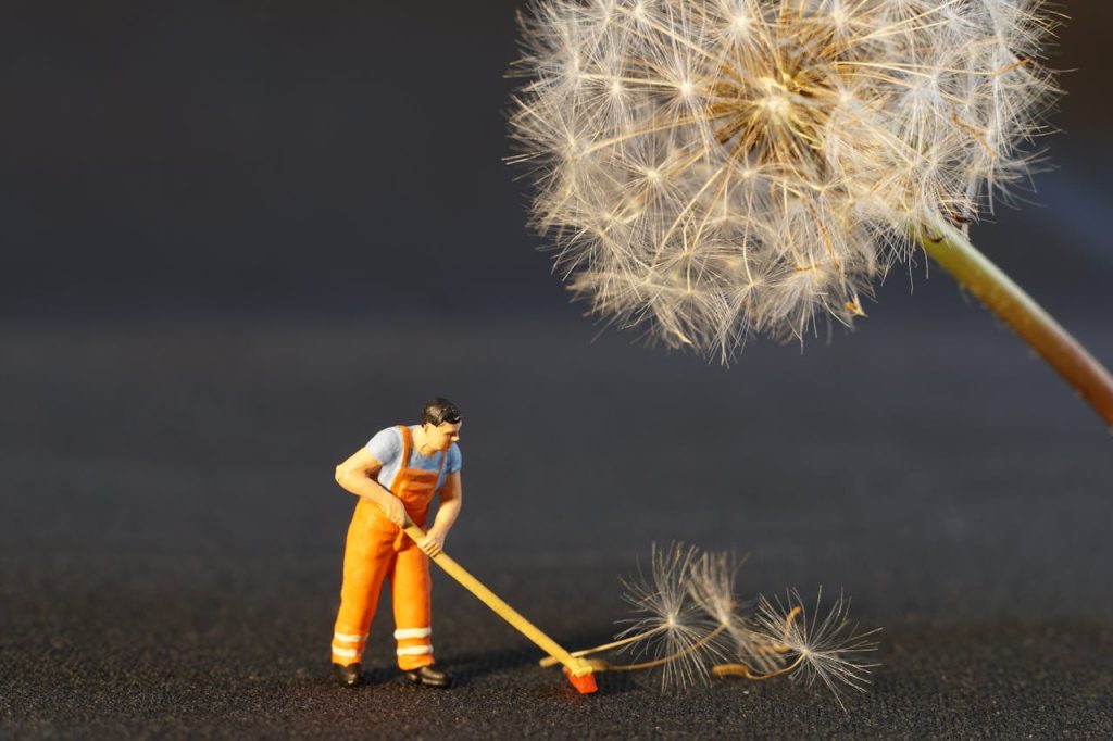 A small figurine of a cleaner sweeping a carpet of dandelion seeds